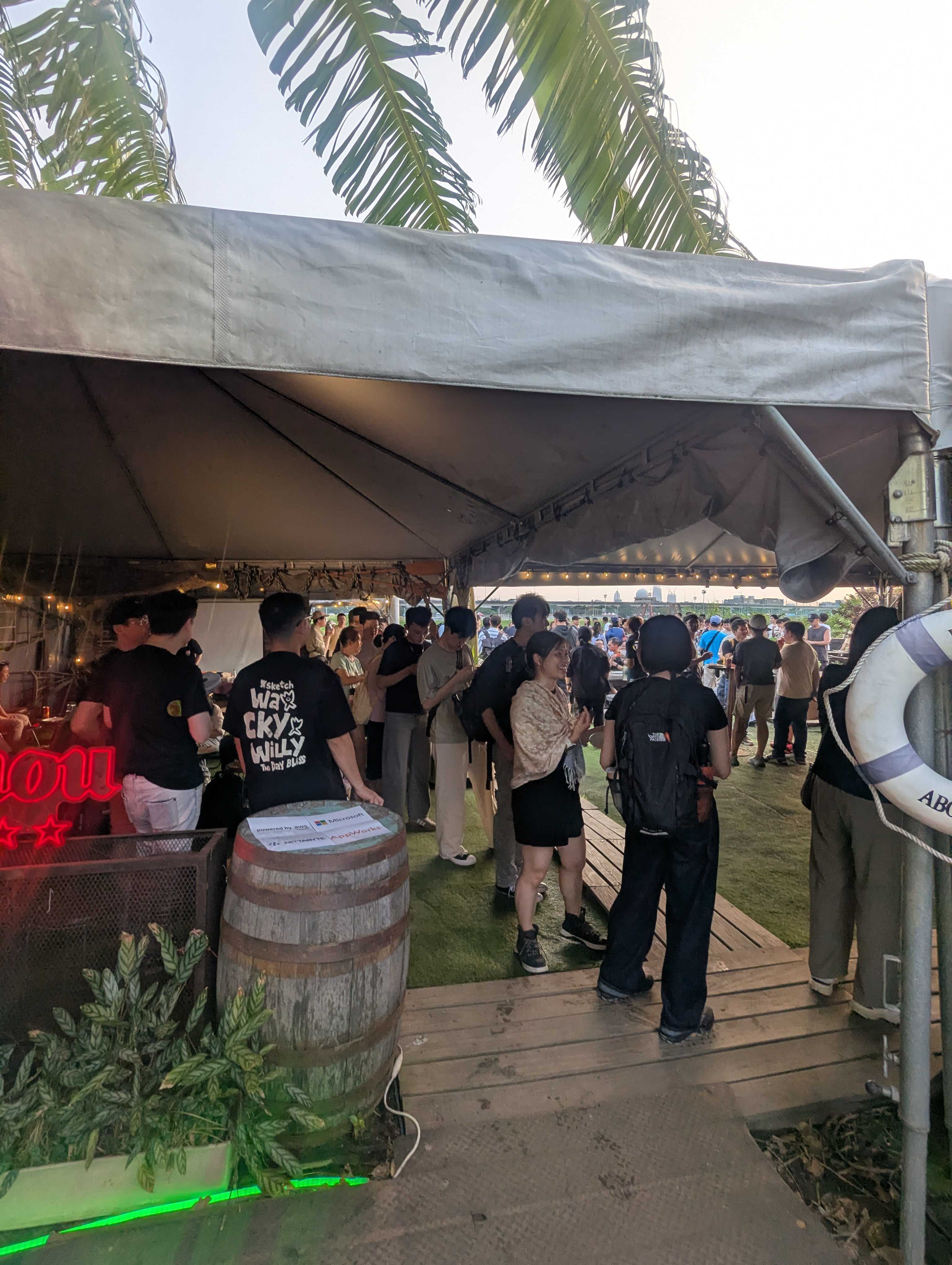 Guests gathering under a tent at the Mid-Autumn Claude Community BBQ in Taipei, with a sponsor sign for AWS, Microsoft, Zettabyte and AppWorks on a barrel.